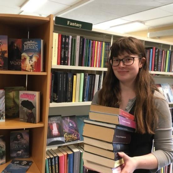 Foto af Katrine med en stak Fantasy-bøger på Skørping Bibliotek