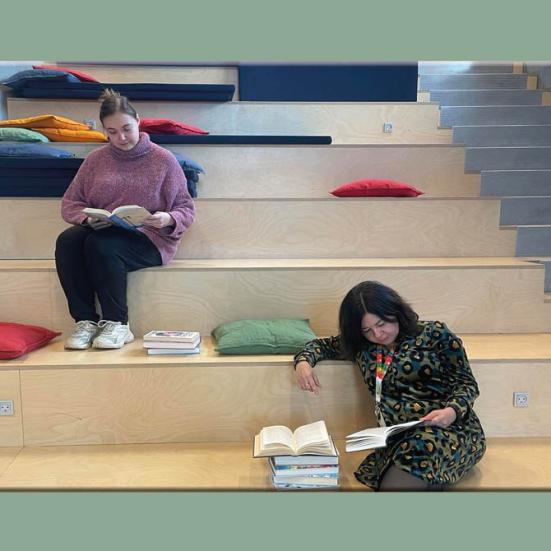 Regitze og Heidi læser bøger på trappen på Støvring Bibliotek